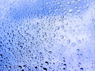 Rain drops on glass. Silhouettes of blue water drops on a transparent surface.