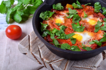 Shakshuka with tomato sauce and quail eggs topped with cilantro in a cast iron pan. Jewish cuisine meal