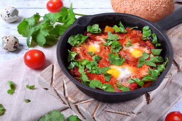 Shakshuka with tomato sauce and quail eggs topped with cilantro in a cast iron pan. Jewish cuisine meal