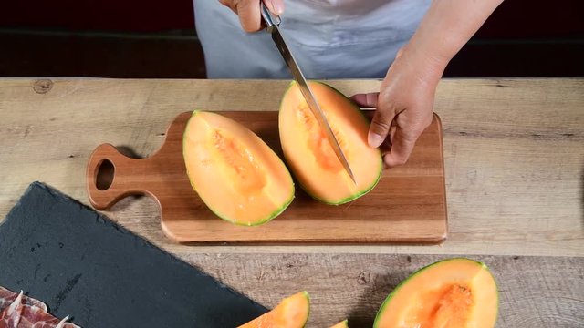 woman cuts fresh melon with knife and wooden chopping board 
