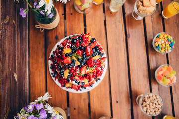 big fruit cake. cake on a wooden background in a rustic style. strawberries, blueberries, currants under the glaze.