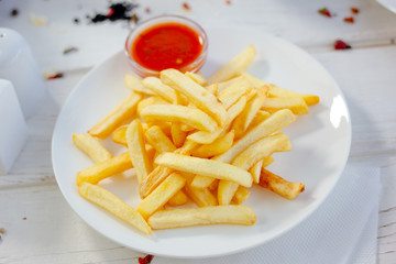 French fries with red tomato sauce on the white plate.