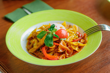 Farfalle pasta with the chicken and tomatoes on a green plate.