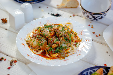 Uyghur lagman with fresh meat and vegetables on white plate.