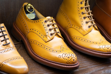 Tan full grain leather brogues shoes set on wooden display in in men shoes boutique store.