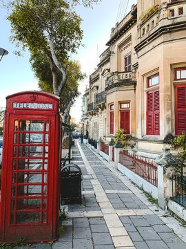 Maltese street with red telephone box in summer. Summer cityscape in Malta. Travel and tourism concept.