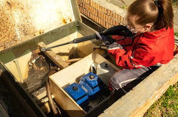 Girl plumber cleans station of biological water purification using a high pressure washer. Sewage...