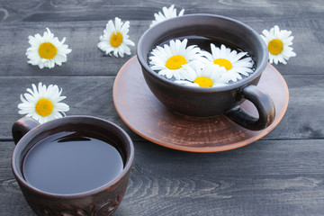 Cup of chamomile tea and chamomile flowers on wooden background.