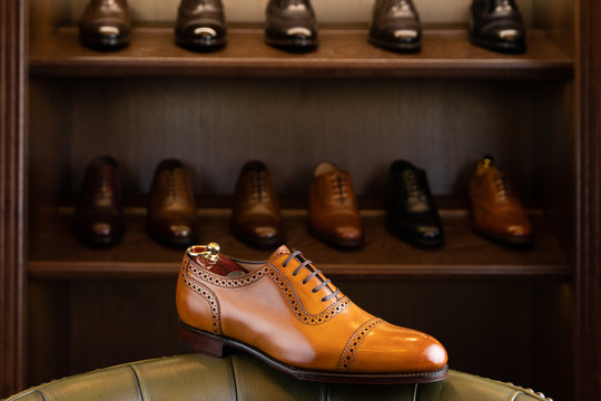Brown full grain leather shoe in front of wooden display in men shoes boutique store.