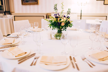served round table with a white tablecloth and flower arrangement. white plate with a napkin and a glass for wine.