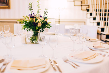 served round table with a white tablecloth and flower arrangement. white plate with a napkin and a glass for wine.