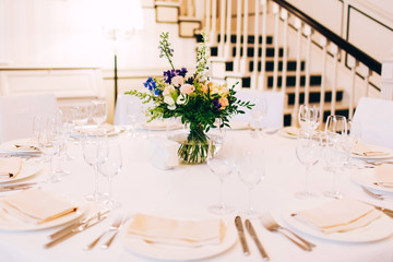 served round table with a white tablecloth and flower arrangement. white plate with a napkin and a glass for wine.