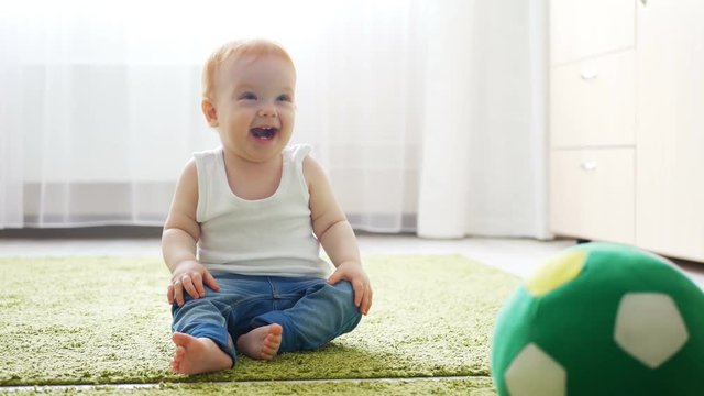 Readhead baby girl playing with a soccer ball on the floor in sunny room