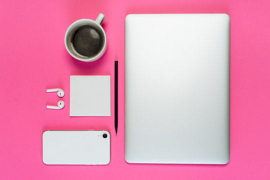 Laptop Phone Coffee Cup on Pink Background Flatlay with Copy Space. White Smartphone, Earphone and Pencil on Minimal Clear Layout Workplace with Paper Note. Business Workspace Inspiration Concept