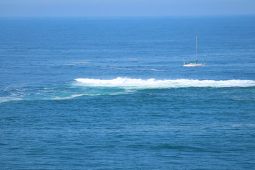 Beautiful blue ocean with the crashing waves and a white yacht 
