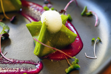 Vegan green raw kimchi dumplings with coconut foam and edible flowers on a black plate