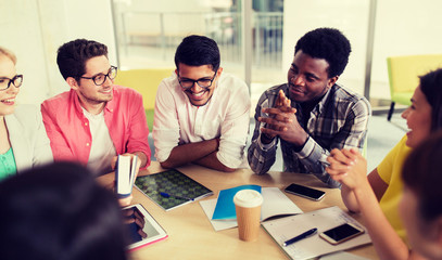 education, high school, people and technology concept - group of international students sitting at table with tablet pc computer, smartphones and notebooks and talking at university