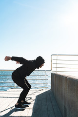 Photo of parkour man doing acrobatics and jumping during morning workout by seaside