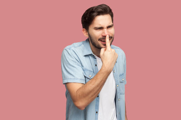 You are liar. Portrait of angry handsome bearded young man in blue casual style shirt standing, touching his nose and showing lie gesture. indoor studio shot, isolated on pink background.