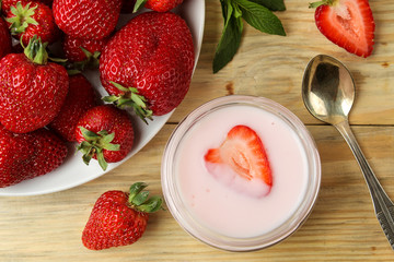 delicious strawberry yogurt in a jar and fresh ripe strawberries on a natural wooden table. top view