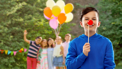 red nose day, party props and photo booth concept - smiling boy in blue hoodie with clown nose over...