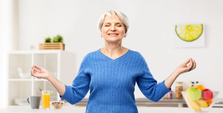 zen, relax and old people concept - portrait of smiling senior woman in blue sweater chilling and meditating over kitchen background