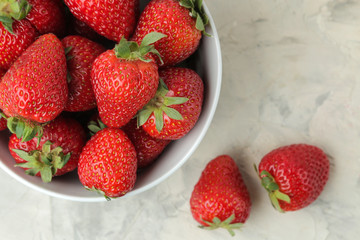 Ripe, delicious strawberries. Red strawberry in a ceramic bowl on a light concrete table. top view