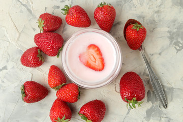delicious strawberry yogurt in a jar and fresh ripe strawberries on a light concrete table. top view