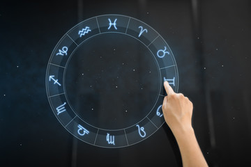 technology, astrology and horoscope concept - hand using interactive panel with signs of zodiac...