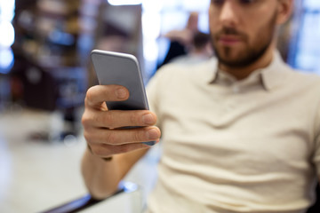 grooming, technology and people concept - close up of man using smartphone at barbershop or hair salon