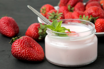 delicious strawberry yogurt in a jar and fresh ripe strawberries and a mint leaf on a black concrete table.