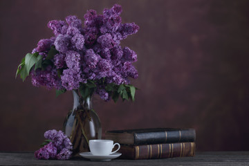 Cup of tea and old books near boquet of lilac flowers