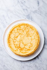 Crepes, thin pancakes on a white plate. Marble background. Copy cpace. Top view.