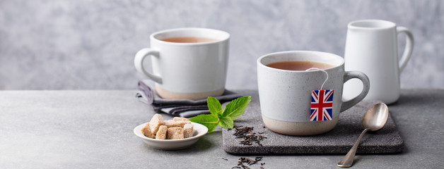 Tea in mugs with British flag tea bag label. Grey background. Copy space.