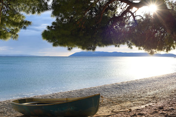 Naklejka na ściany i meble Wooden boat on the Adriatic coast. Against the backdrop of the sunset and beautiful big pine in Croatia