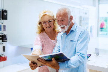 Fototapeta premium Cute smiling Caucasian senior couple looking at catalog in tech store.