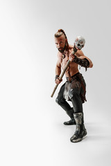 Serious long hair and muscular male model in leather viking's costume with the big mace cosplaying isolated on white studio background. Full-length portrait. Fantasy warrior, antique battle concept.