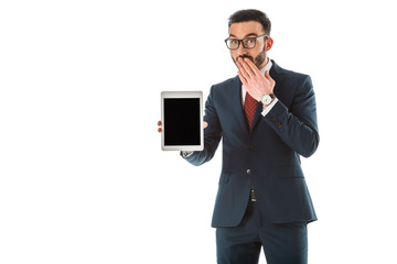 surprised businessman holding digital tablet with blank screen and covering mouth with hand isolated on white
