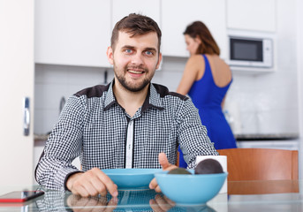 Fototapeta na wymiar Young man sitting at kitchen table, woman preparing food