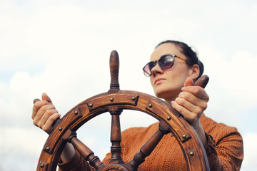 The girl controls the yacht, hands on the steering wheel,  handwheel on sky background