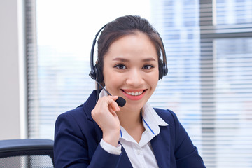 Portrait of happy smiling female customer support phone operator at workplace. Asian
