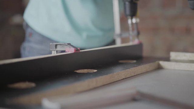 Carpenter making halls in the chipboard details with cordless screwdriver. Concept of hand manufacturing. Craftman works in a workshop.