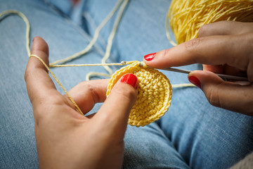 Girl doing crochet with yellow yarn and nails painted red