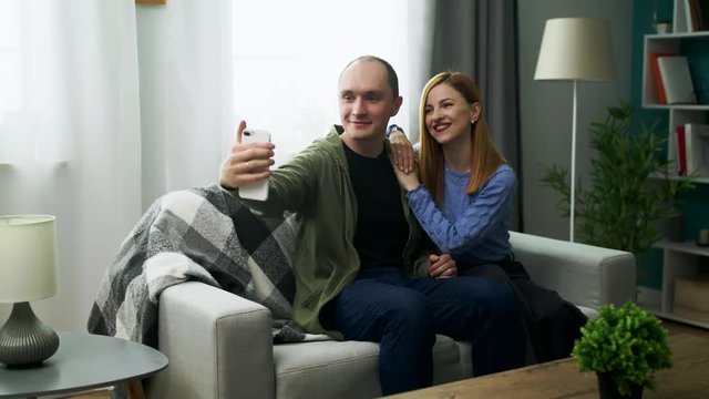 Young man taking selfie on phone camera with his girlfriend in the living room