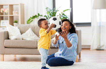 childhood, kids and people concept - happy african american mother and her baby son playing with soccer ball together on sofa at home