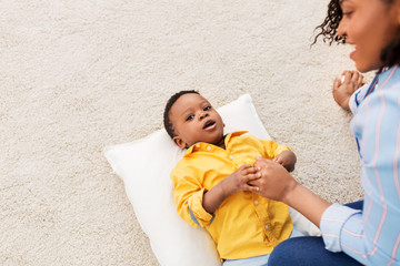 childhood, kids and people concept - happy african american mother with her baby son lying on pillow at home