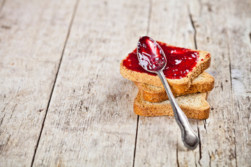 Toasted cereal bread slices stack with homemade cherry jam and spoon closeup on rustic wooden table...