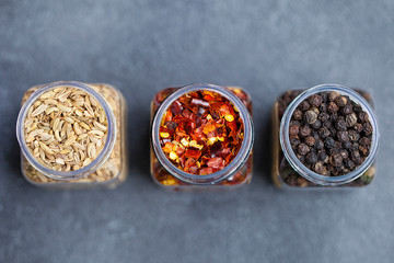 Obraz na płótnie Canvas Spices in jars, fennel, chili pepper flakes, black peppercorns. Slate background. Top view. Copy space.