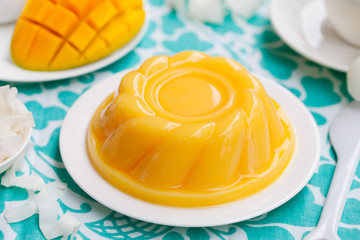 Mango pudding, jelly, dessert on white plate with fresh fruit. Colorful textile background.