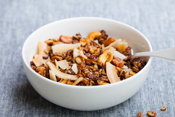 Fresh granola, muesli with coconut, banana and nuts in a white bowl. Grey background.